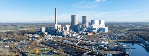 Eine Luftaufnahme eines Kraftwerks mit Kühltürmen, Industriegebäuden und umliegenden grünen Feldern.