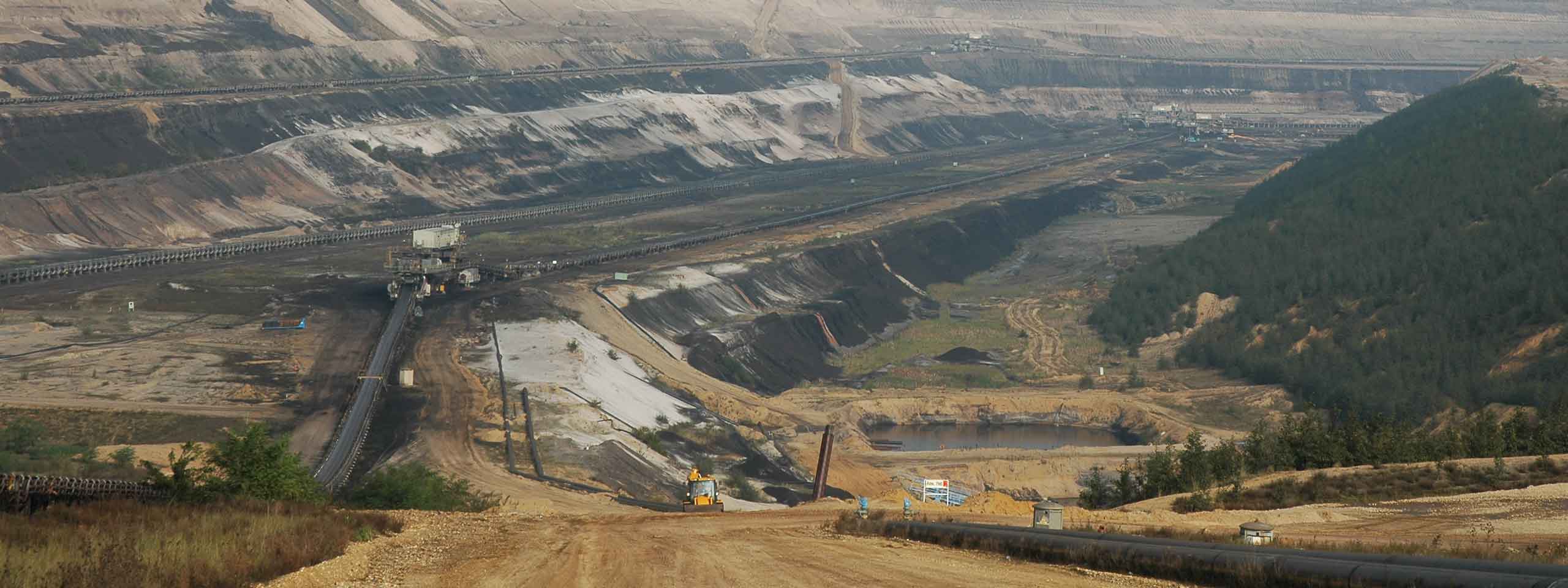 Ein riesiges Tagebaugebiet mit steilen Hängen, Maschinen und gewundenen Förderbändern in einer rauen Landschaft.