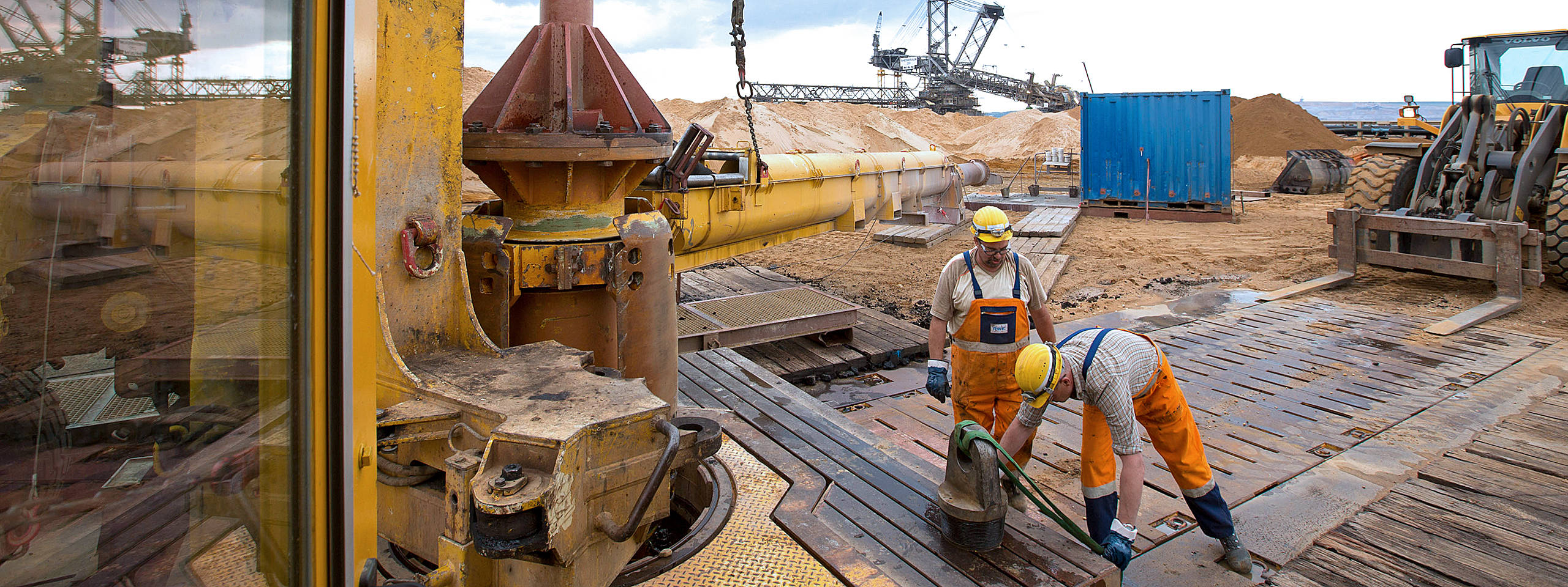 Bauarbeiter arbeiten an einer Baustelle mit schwerem Gerät und Sand im Hintergrund.