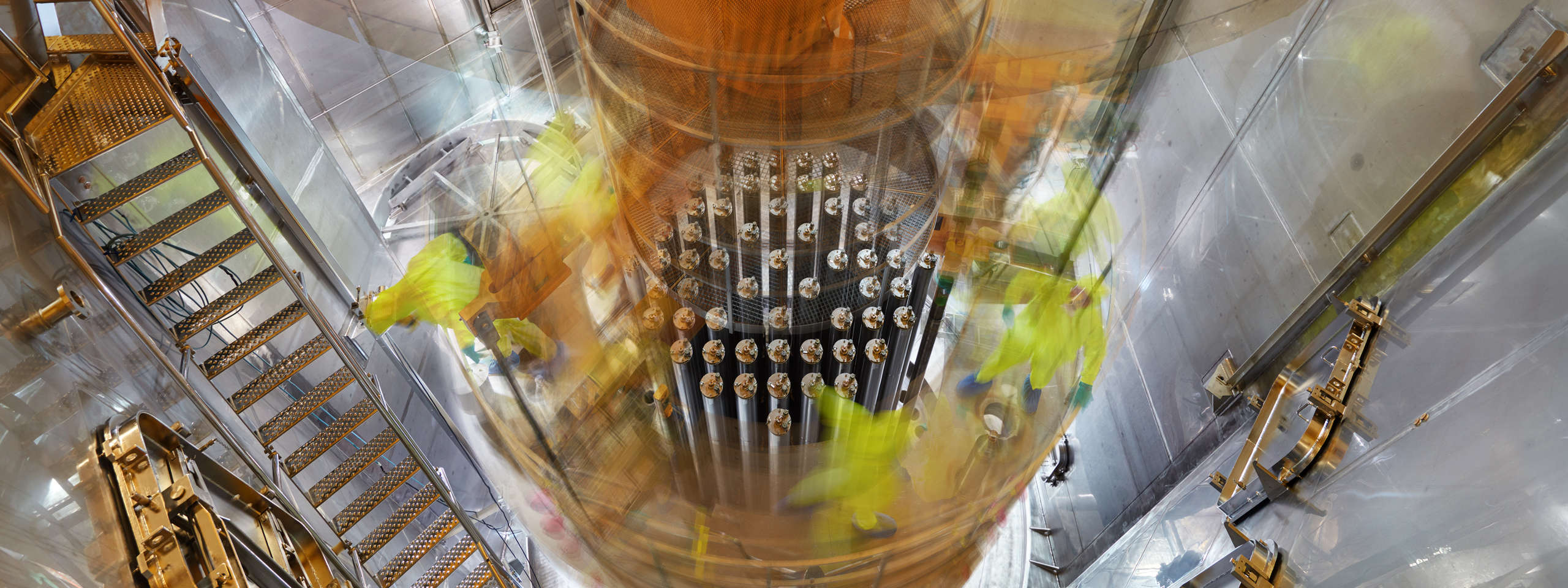 Ein Blick auf einen Reaktorkernbereich mit Arbeitern in gelben Anzügen und sichtbaren Metallstrukturen.