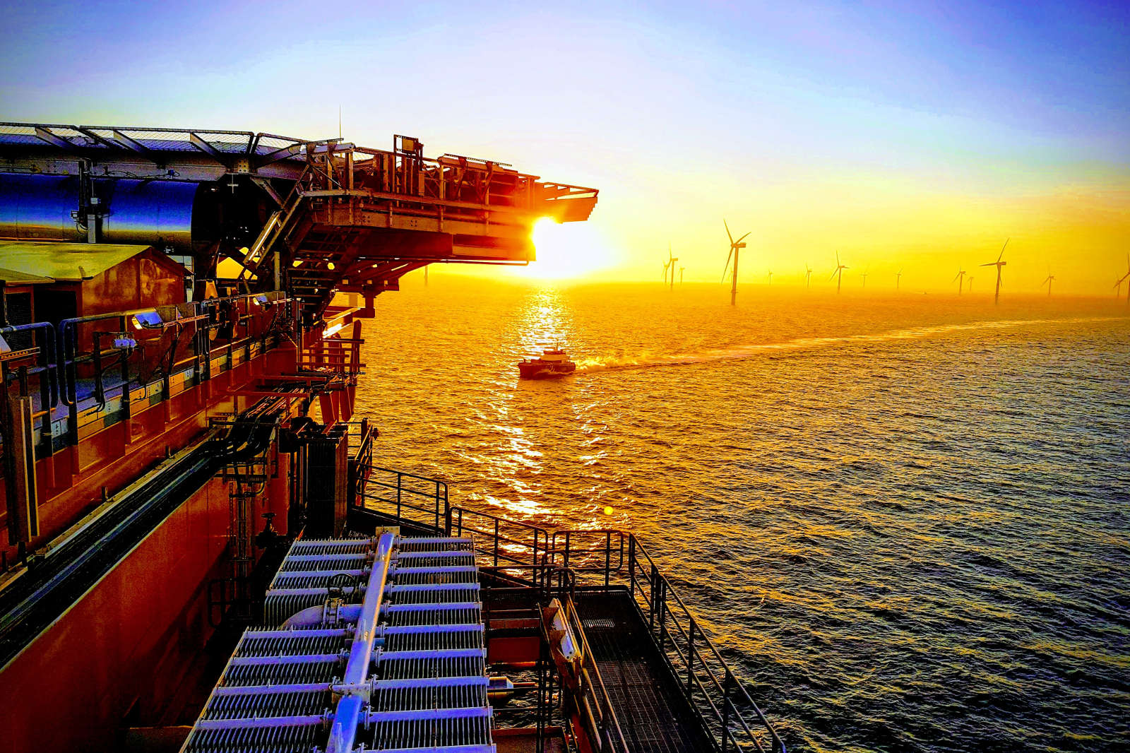 Ein Sonnenuntergang über dem Meer, mit einem Schiff und Windkraftanlagen im Hintergrund.