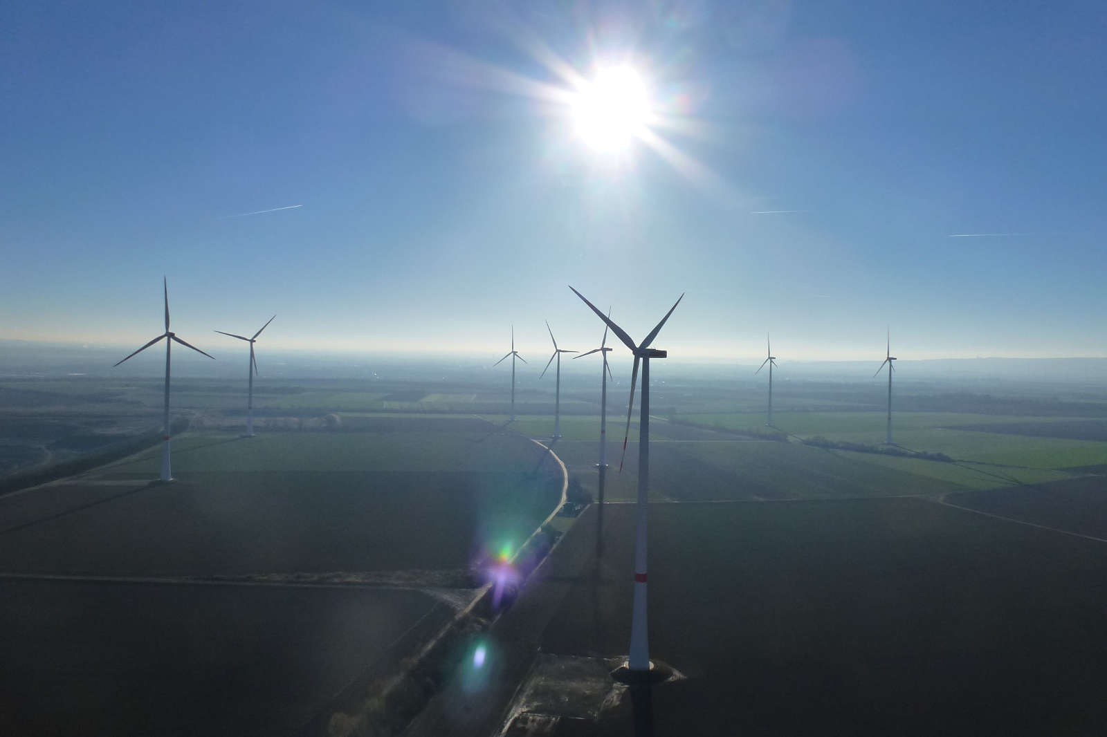 Luftaufnahme von Windkraftanlagen in einem weiten Feld unter einem klaren Himmel und strahlender Sonne.