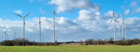 Weitläufige Landschaft mit vielen Windkraftanlagen und einem klaren blauen Himmel mit Wolken.