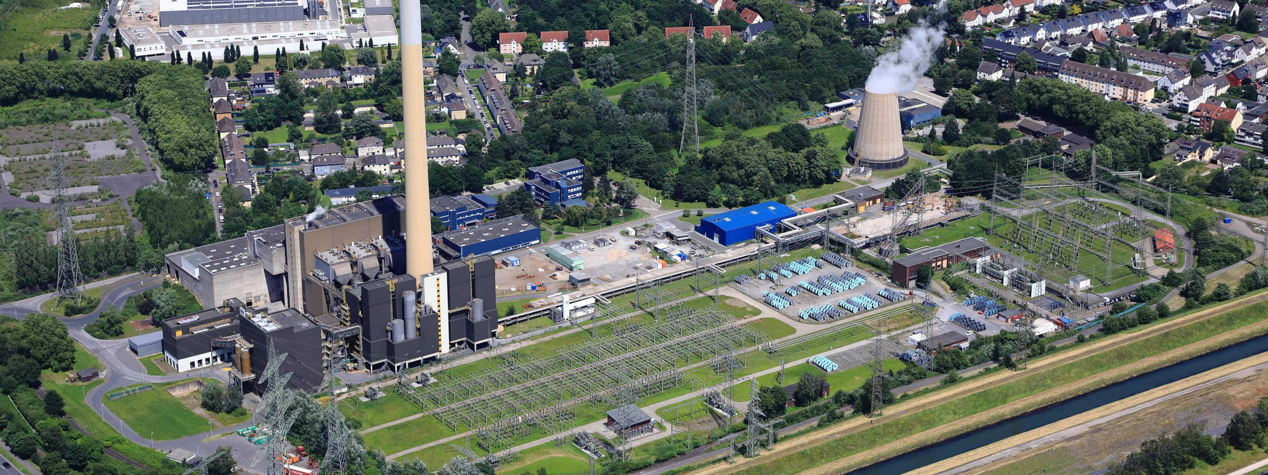 Luftaufnahme eines Industriegebiets mit einem Kraftwerk, Kühlturm, Stromleitungen und benachbarten Wohngebieten.
