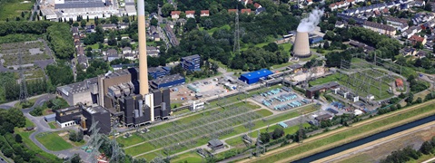 Luftaufnahme eines Industriegebiets mit einem Kraftwerk, Kühlturm, Stromleitungen und benachbarten Wohngebieten.