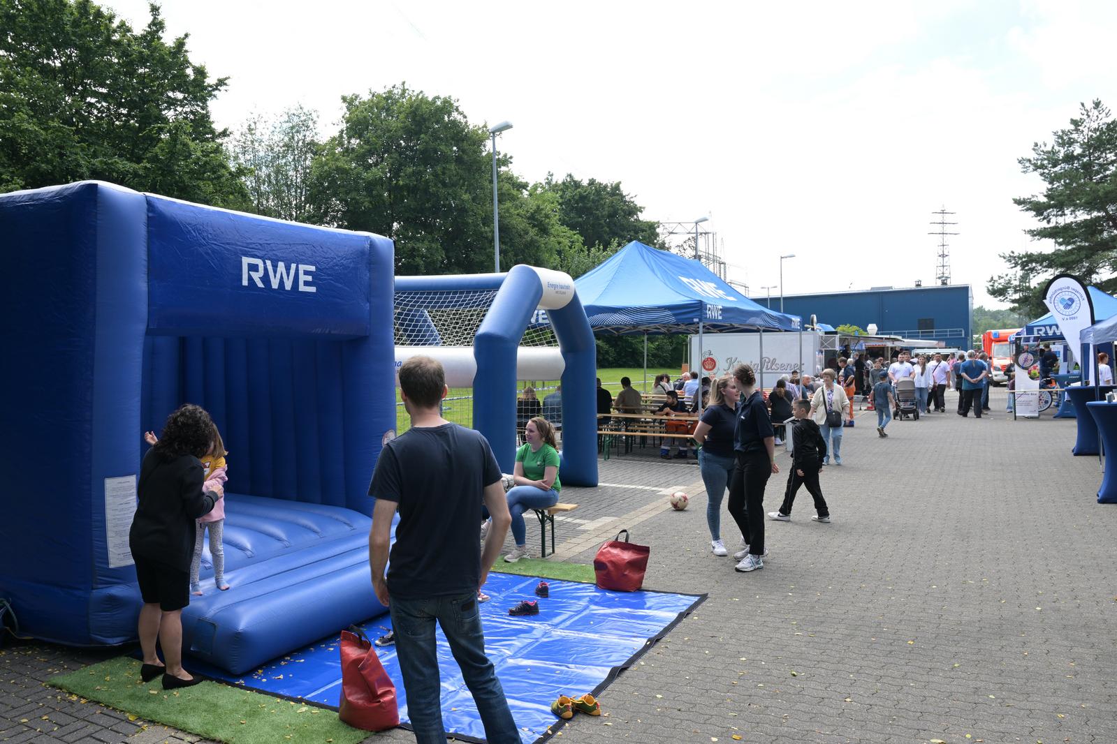 Eine lebhafte Outdoor-Veranstaltung mit einem blauen aufblasbaren Hüpfhaus, Essensständen und Besuchern, die die Aktivitäten genießen.