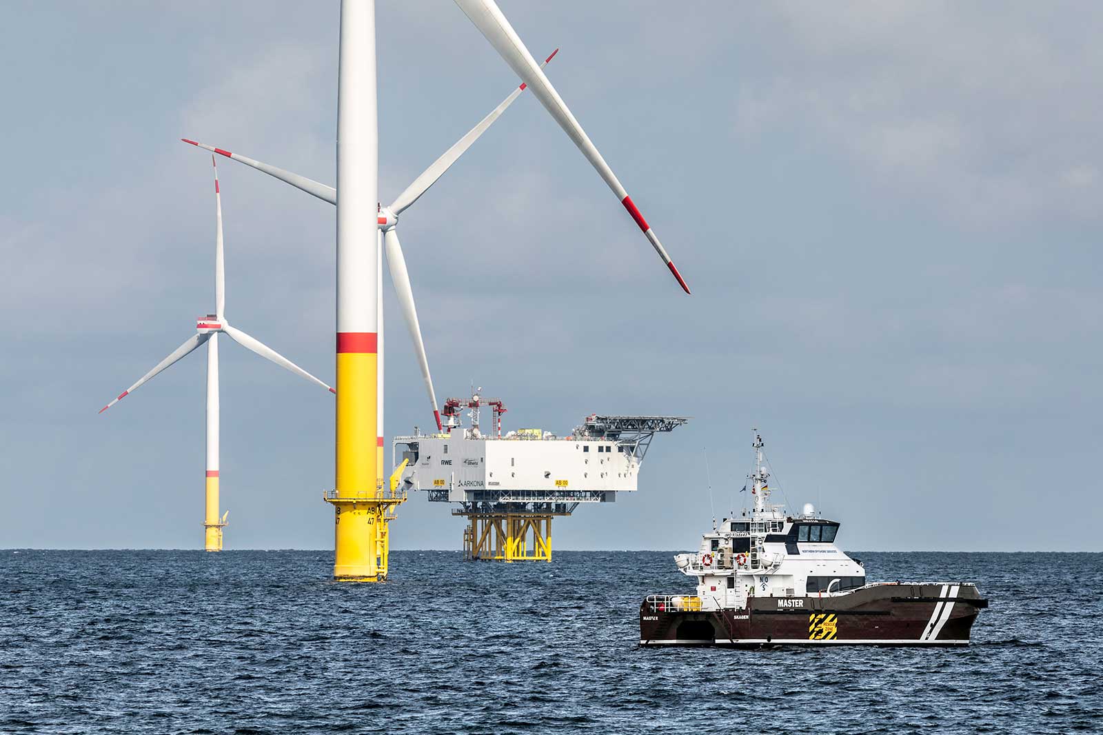 Offshore-Windkraftanlagen mit einem Schiff im Vordergrund auf dem offenen Wasser unter einem bewölkten Himmel.