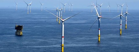 Eine Reihe von Windkraftanlagen auf dem Meer vor einem blauen Himmel. Im Vordergrund steht eine Plattform.