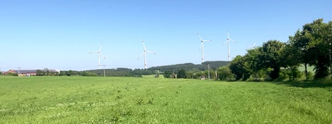 Ein grünes Feld mit mehreren Windkraftanlagen im Hintergrund unter einem klaren blauen Himmel.