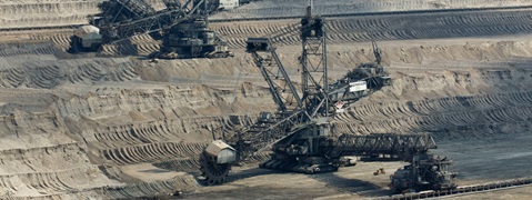 Eine Luftansicht großer Bagger, die in einem weitläufigen, sandigen Bergbaugebiet mit ausgeprägten Erdschichten arbeiten.