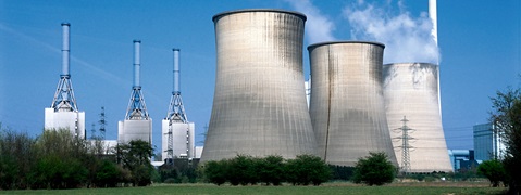 A view of a power plant featuring cooling towers and tall smokestacks against a blue sky.