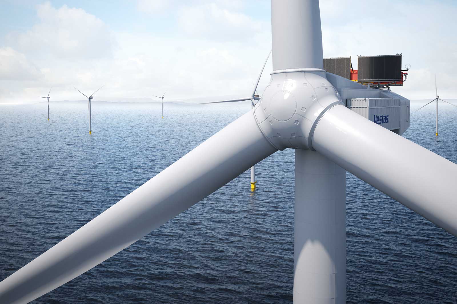 A close-up of a wind turbine with a view of the sea and several wind turbines in the background.