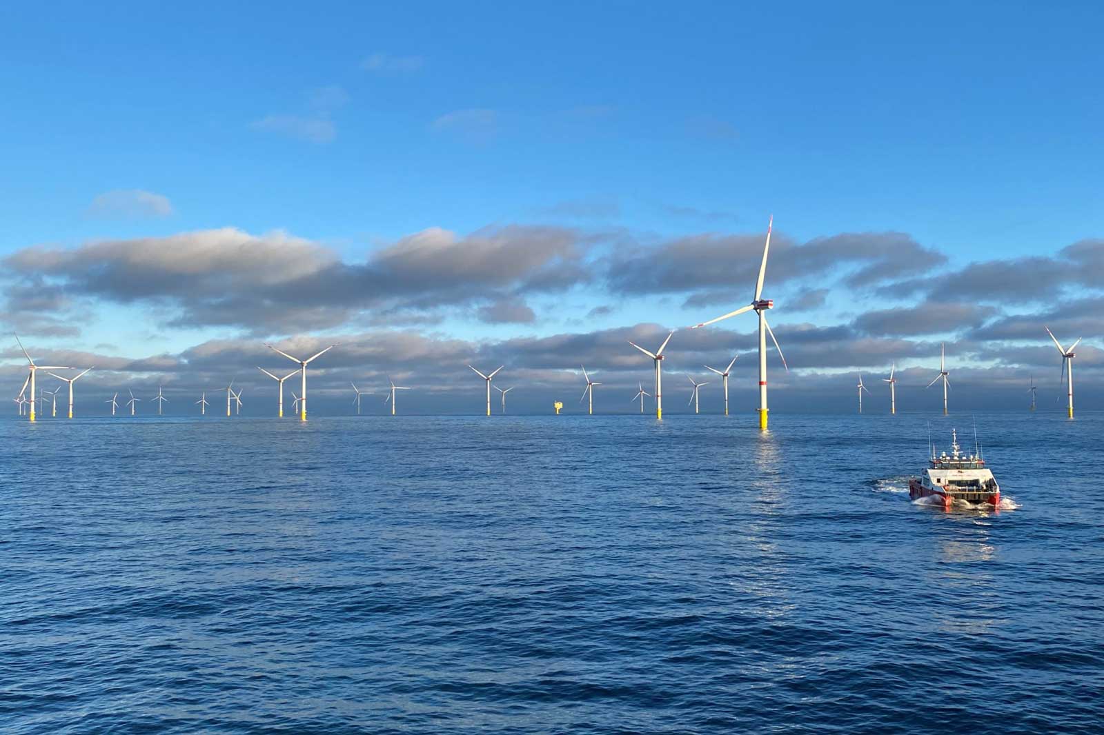 A boat navigates through calm waters near offshore wind turbines under a partly cloudy sky.