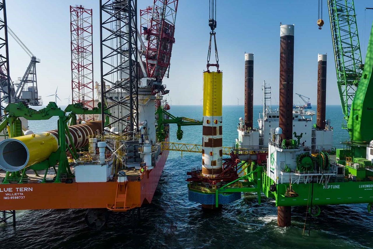 A view of two offshore construction vessels working together, with a yellow cylindrical structure being lifted over the water.
