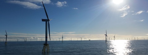 Ein Blick auf mehrere Windturbinen im Ozean, beleuchtet von hellem Sonnenlicht, mit klarem blauen Himmel und sanften Wellen.