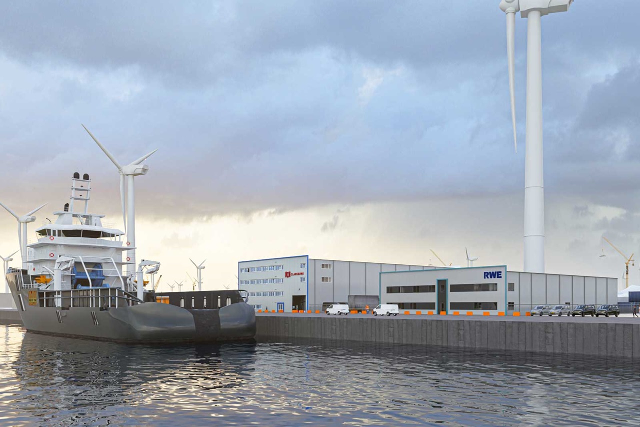 Ein Schiff liegt an einem Hafen mit Windkraftanlagen und Lagerhäusern im Hintergrund. Die Wasseroberfläche spiegelt die Umgebung wider.