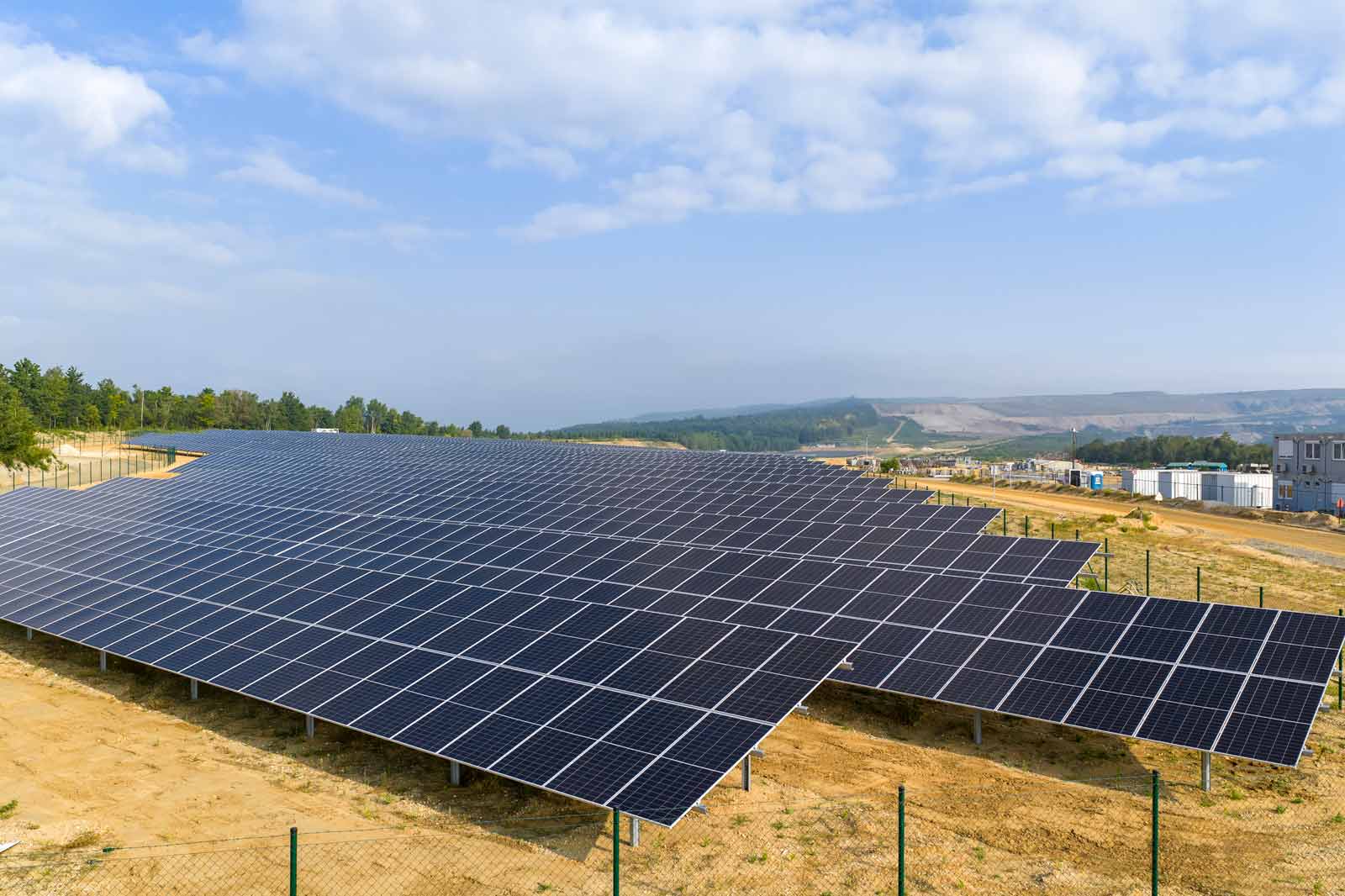 Eine große Solarfarm mit zahlreichen Solarpanelen, die in langen Reihen auf unebenem Gelände angeordnet sind.