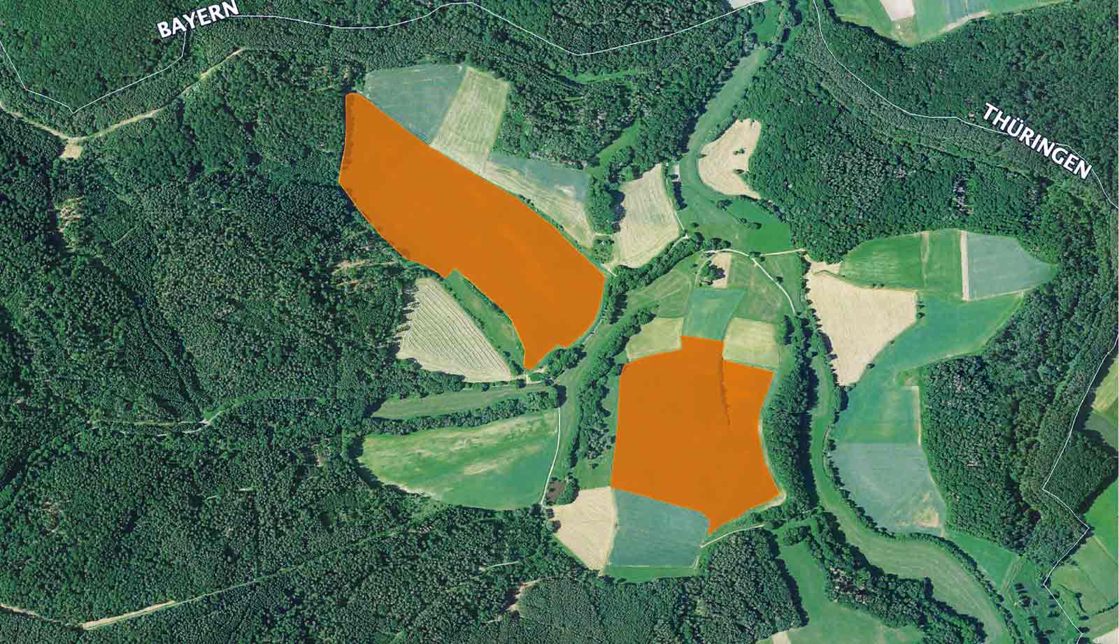 Luftaufnahme einer ländlichen Landschaft mit grünen Feldern und orange markierten Flächen, umgeben von Waldgebieten.