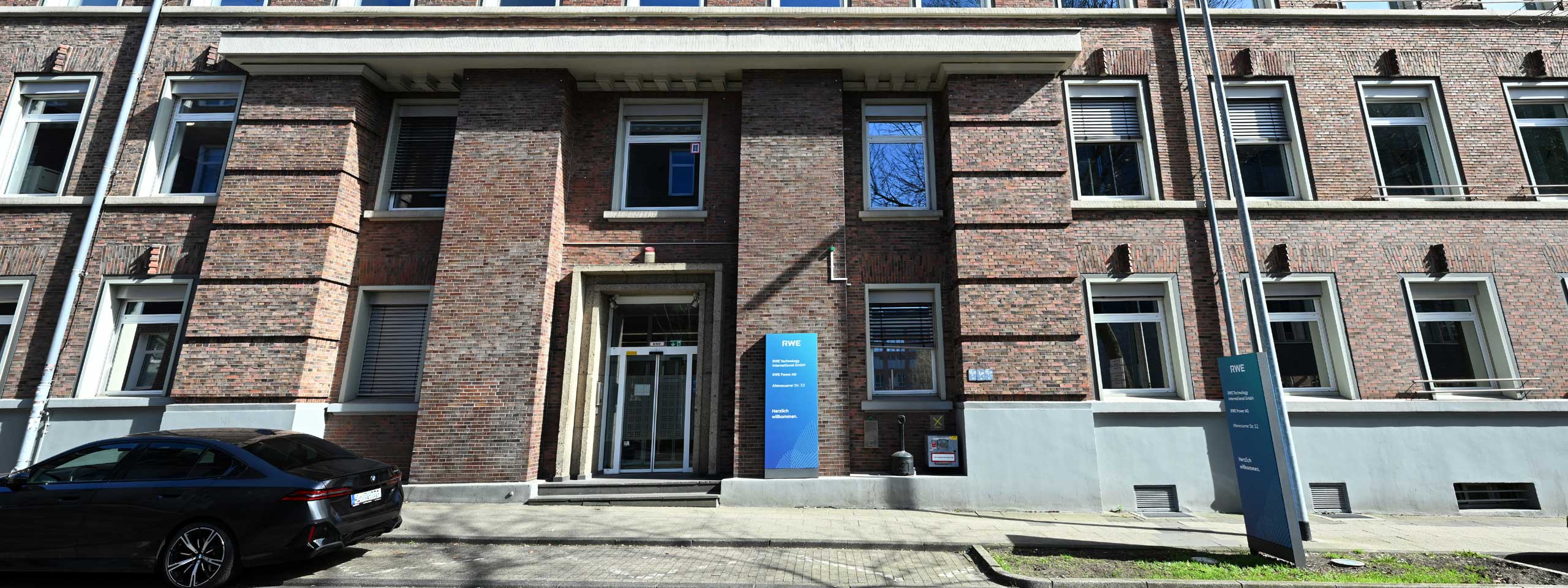 A modern brick office building with large windows and a glass entrance. A black car is parked in front.
