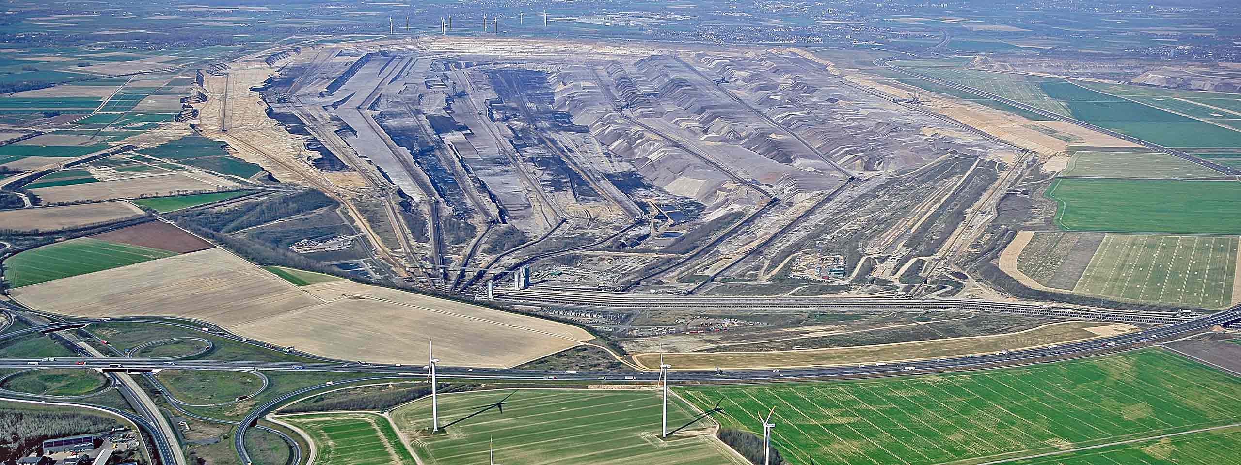 Aerial view of a large opencast mine with terraced earth formations and surrounding fields.