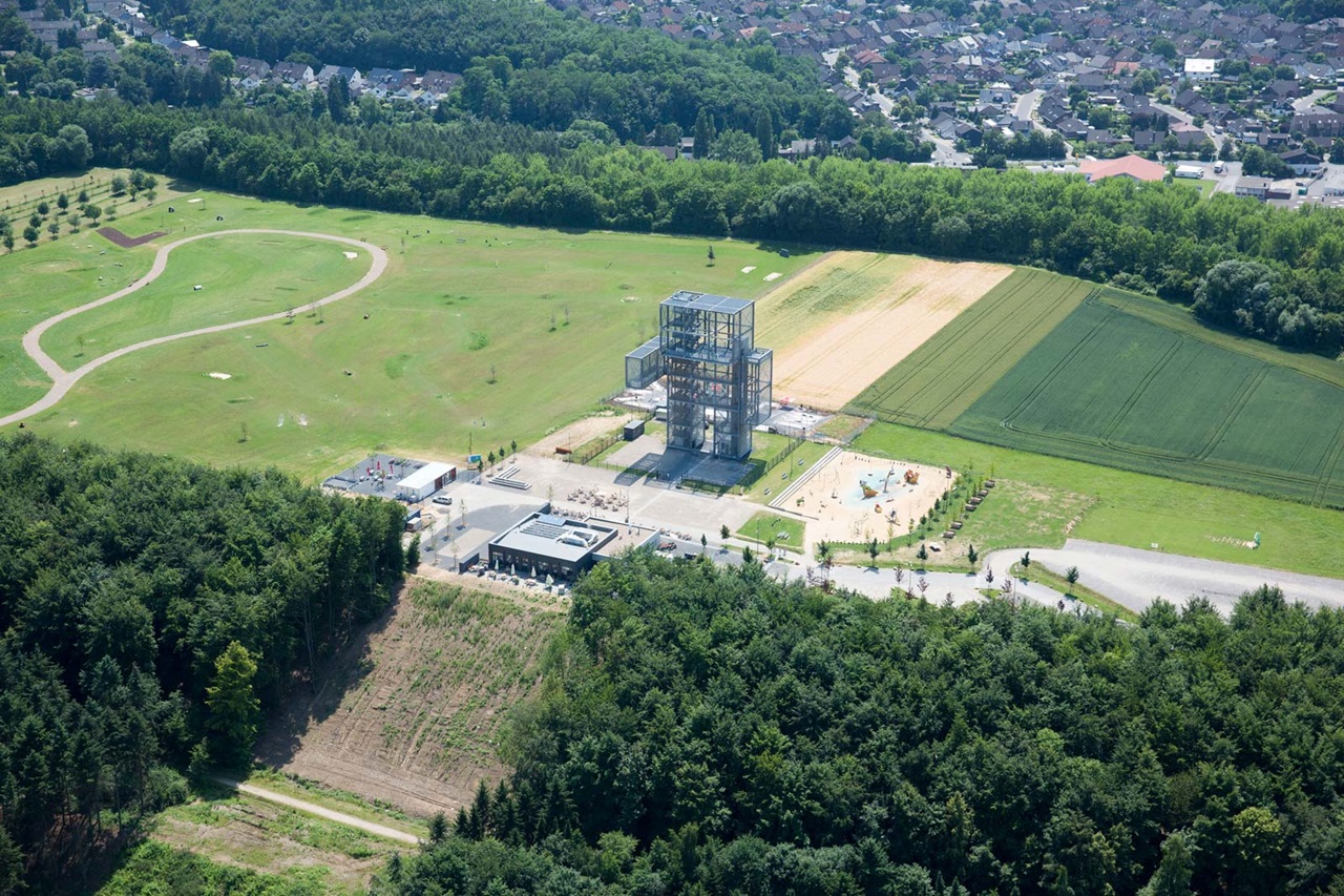 An aerial view of a modern building surrounded by a park, fields, and forests.