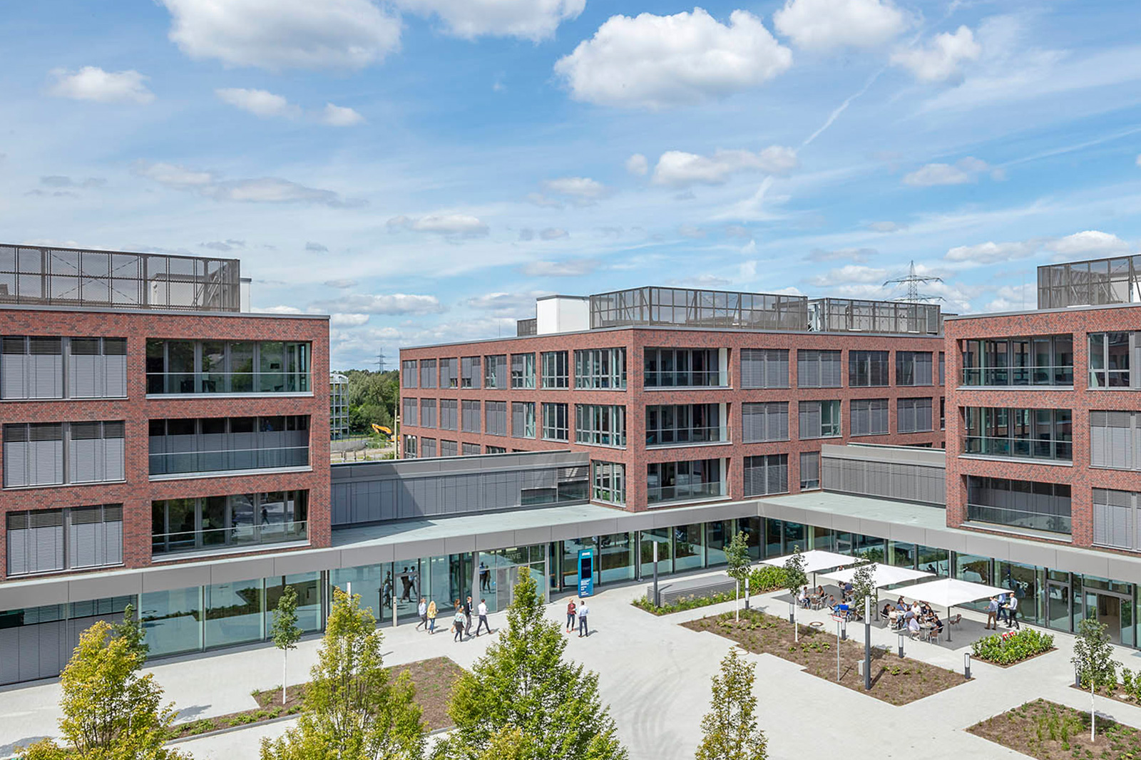 Moderne Bürogebäude mit roten Backsteinfassaden und einem Innenhof, in dem Menschen arbeiten und sich entspannen.