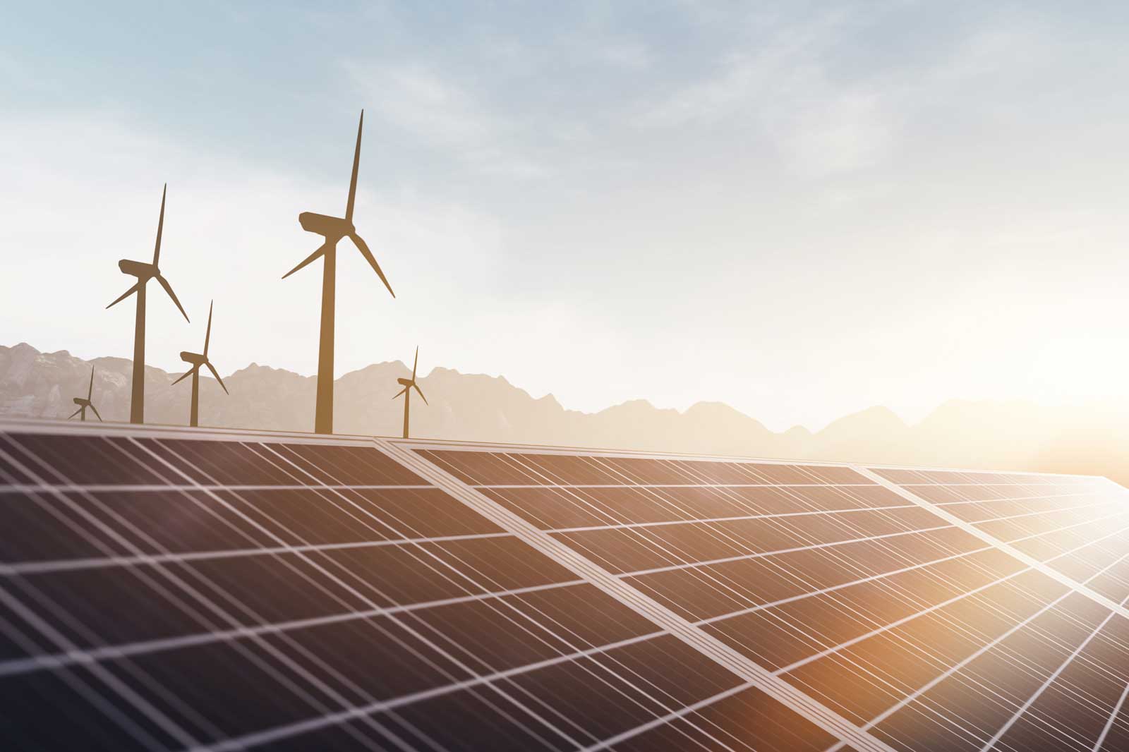 Solarpanel mit Windkraftanlagen im Hintergrund, bei Sonnenuntergang, vor einer bergigen Landschaft.