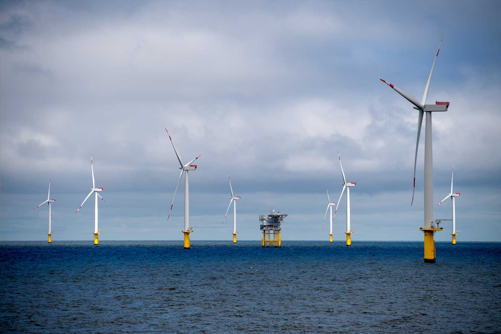 A wind farm with several turbines on stilts in the ocean under a cloudy sky.