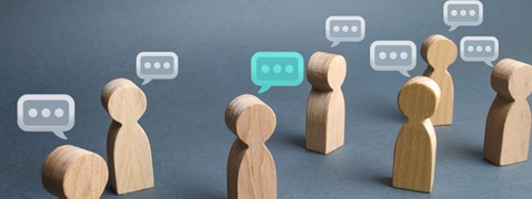 Holzfiguren stehen in einer Gruppe und kommunizieren, dargestellt durch Sprechblasen über ihnen.