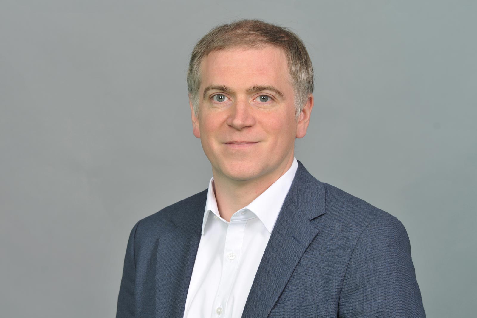 A man in a grey suit and white shirt poses against a grey background. Portrait of Bernhard Wurm.