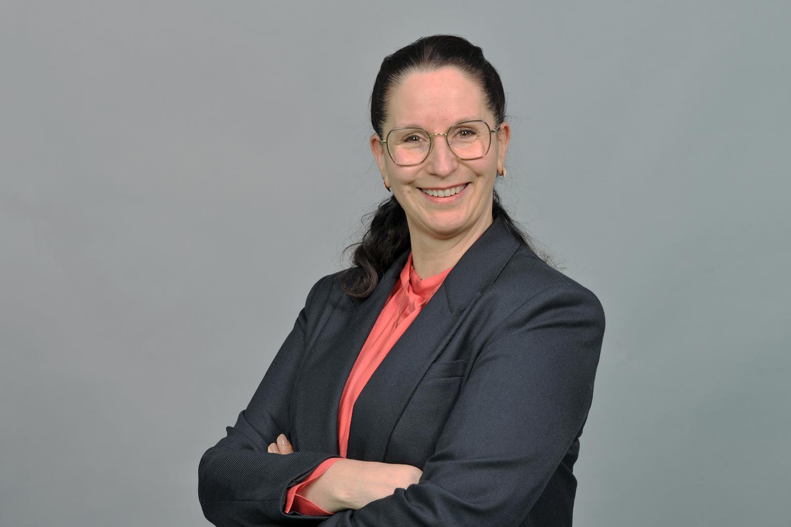 A woman with dark hair is wearing a black blazer and a red top. She has her arms crossed. Portrait of Melanie Kleemann.
