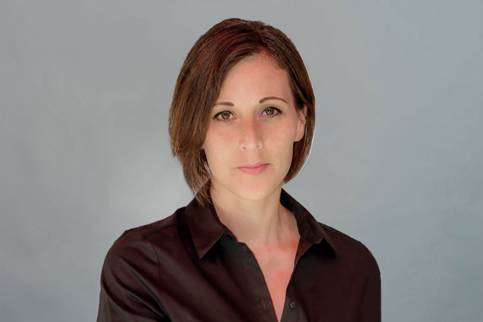 A person with shoulder-length hair is wearing a black shirt, standing against a grey background. Portrait of Natalie Henßen.