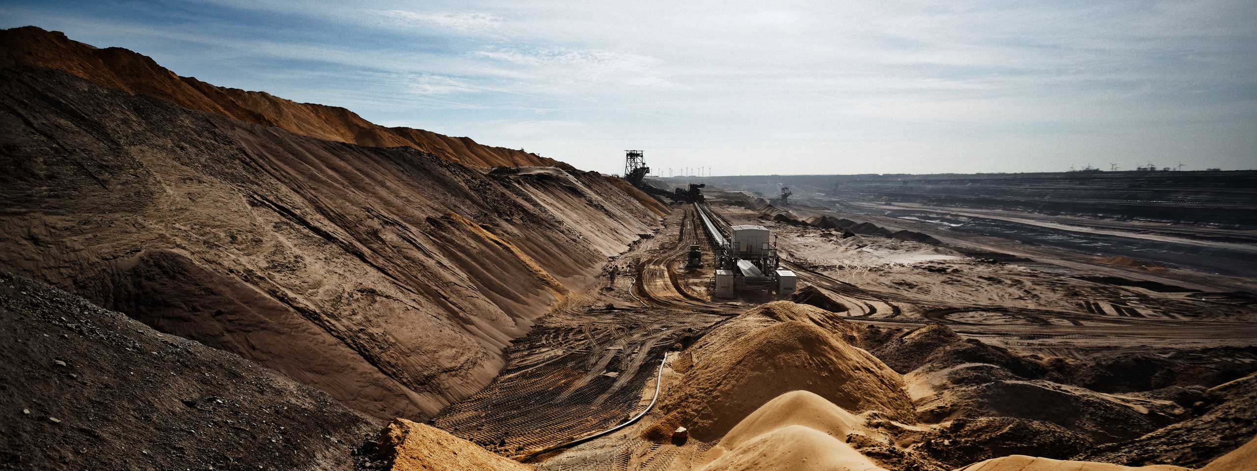 An industrial landscape featuring large hills of sand and earth, conveyor belts, and machinery in an open-pit mining site.