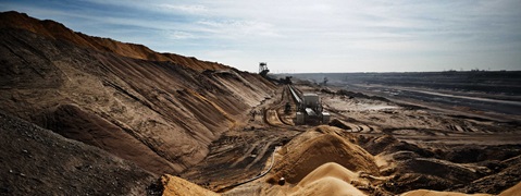 An industrial landscape featuring large hills of sand and earth, conveyor belts, and machinery in an open-pit mining site.
