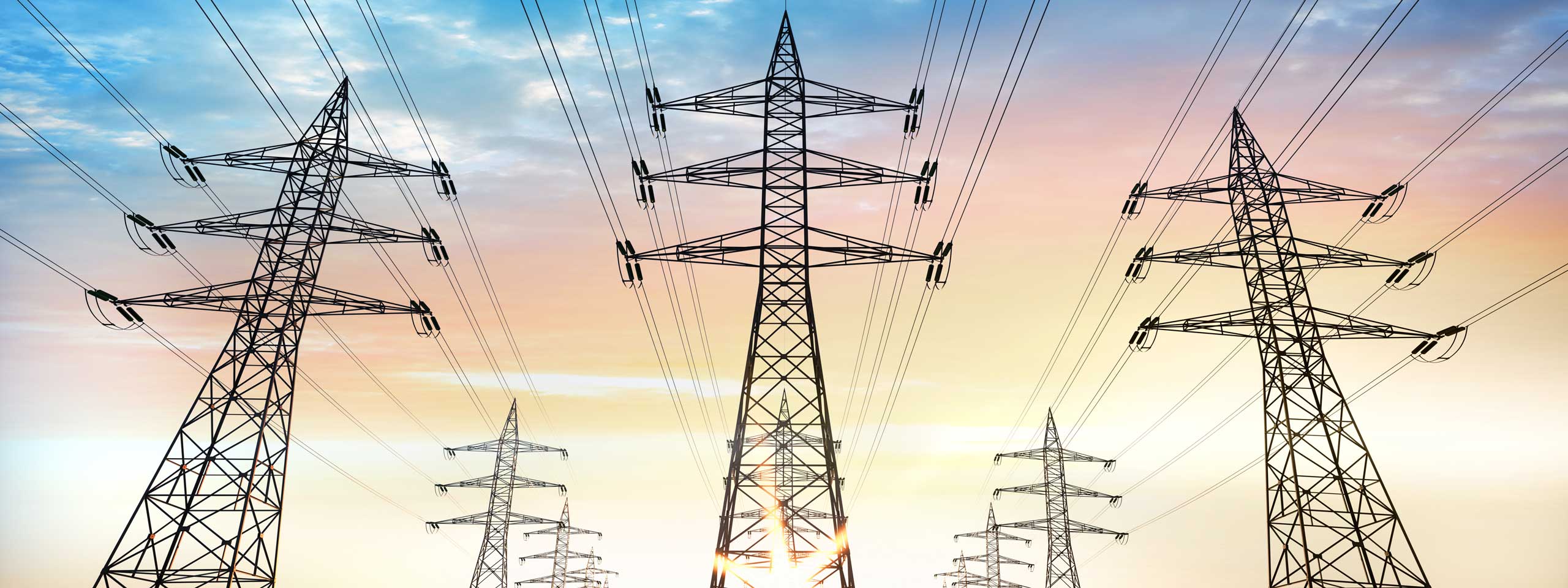 High voltage pylons stand against a colourful sky at sunset.