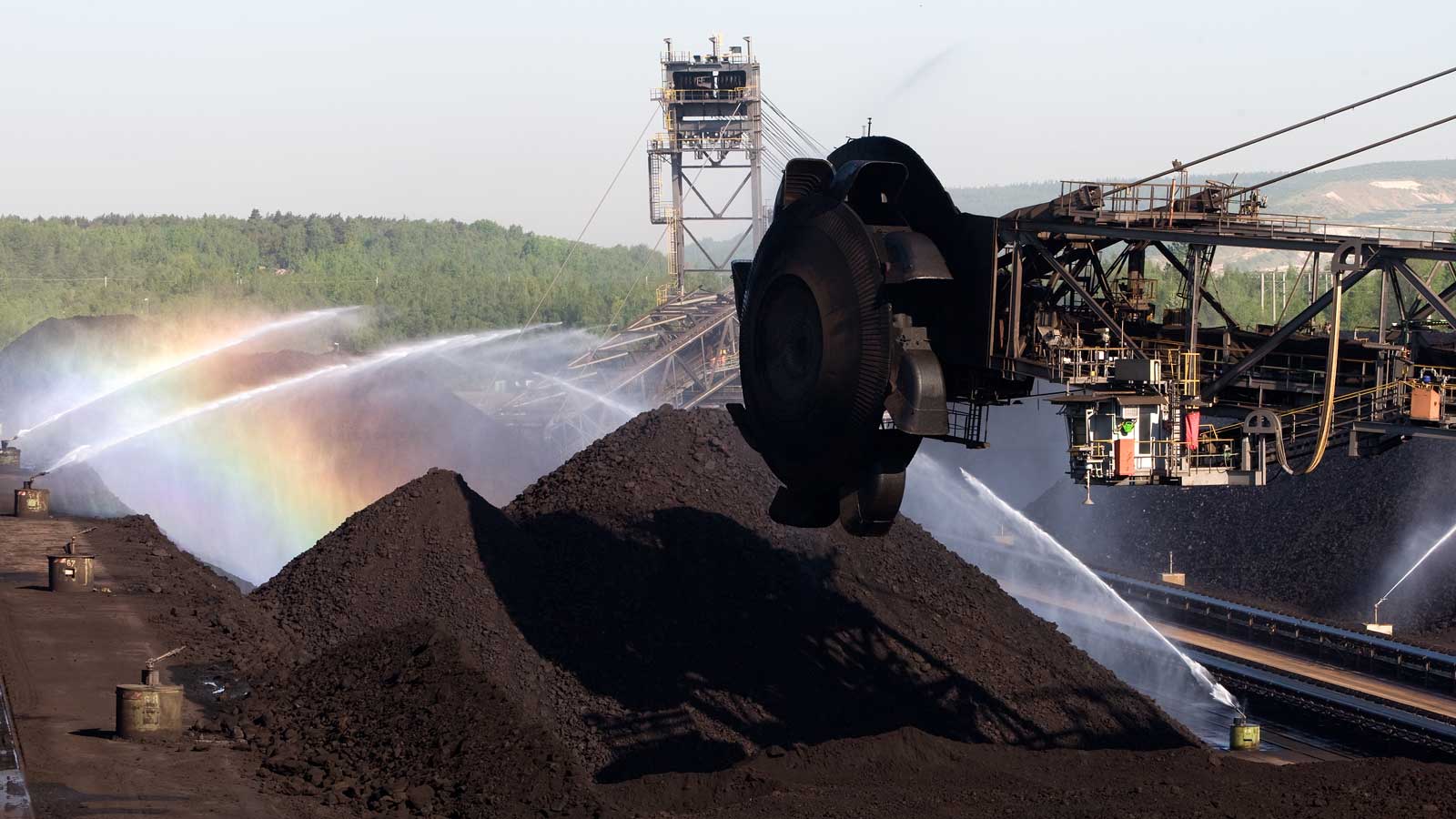 A coal mine with large heaps of coal, water spraying creates a rainbow in the sunlight.