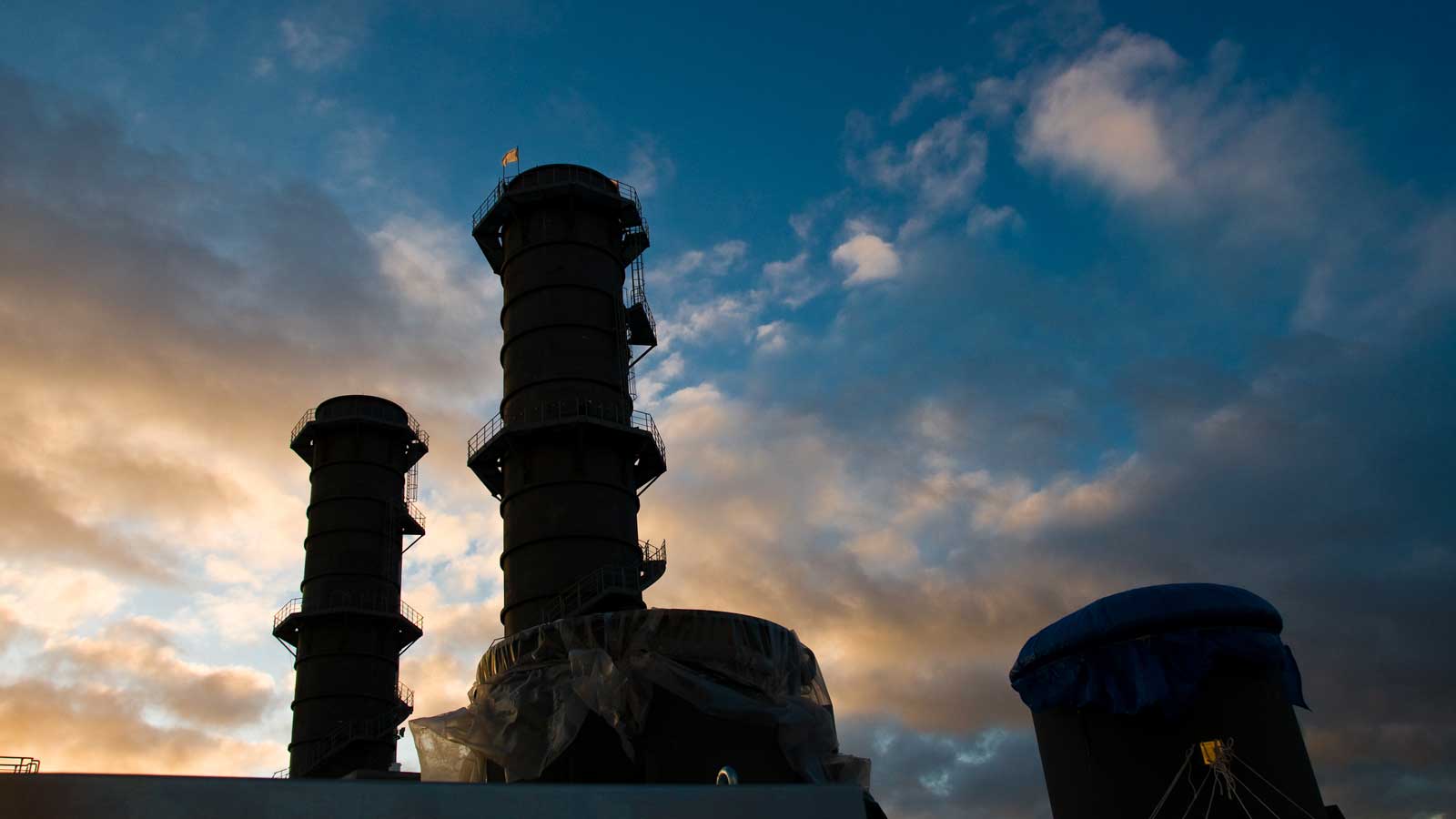 Dark silhouettes of tall chimneys against a colourful sky at sunset.