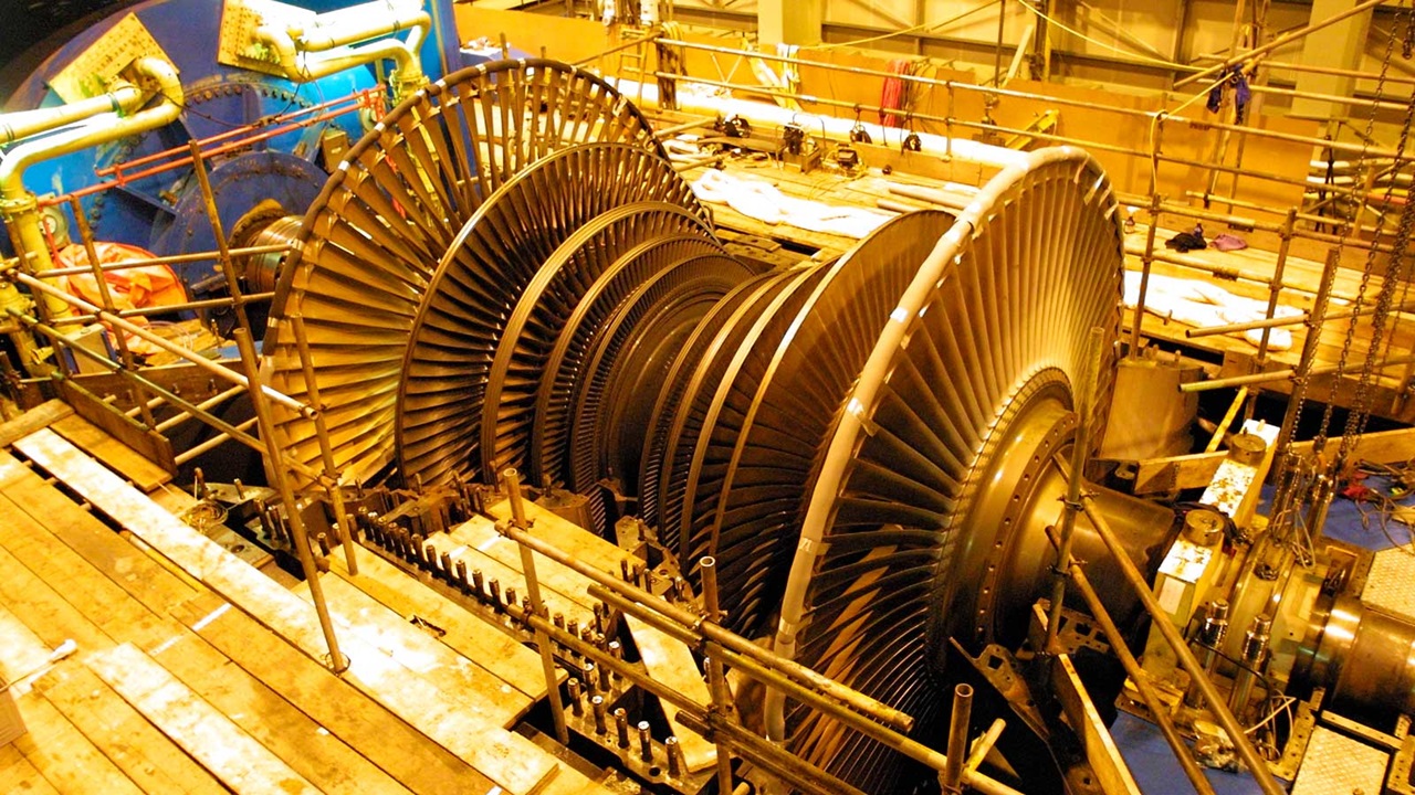 Eine große Turbine mit vielen Schaufeln, umgeben von Gerüsten in einer industriellen Umgebung.