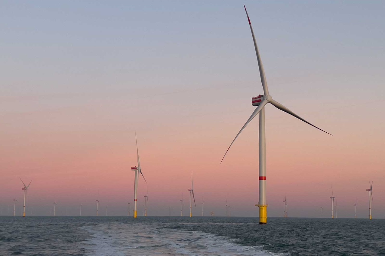 Several wind turbines stand majestically in the water against a soft pink sky at sunset.