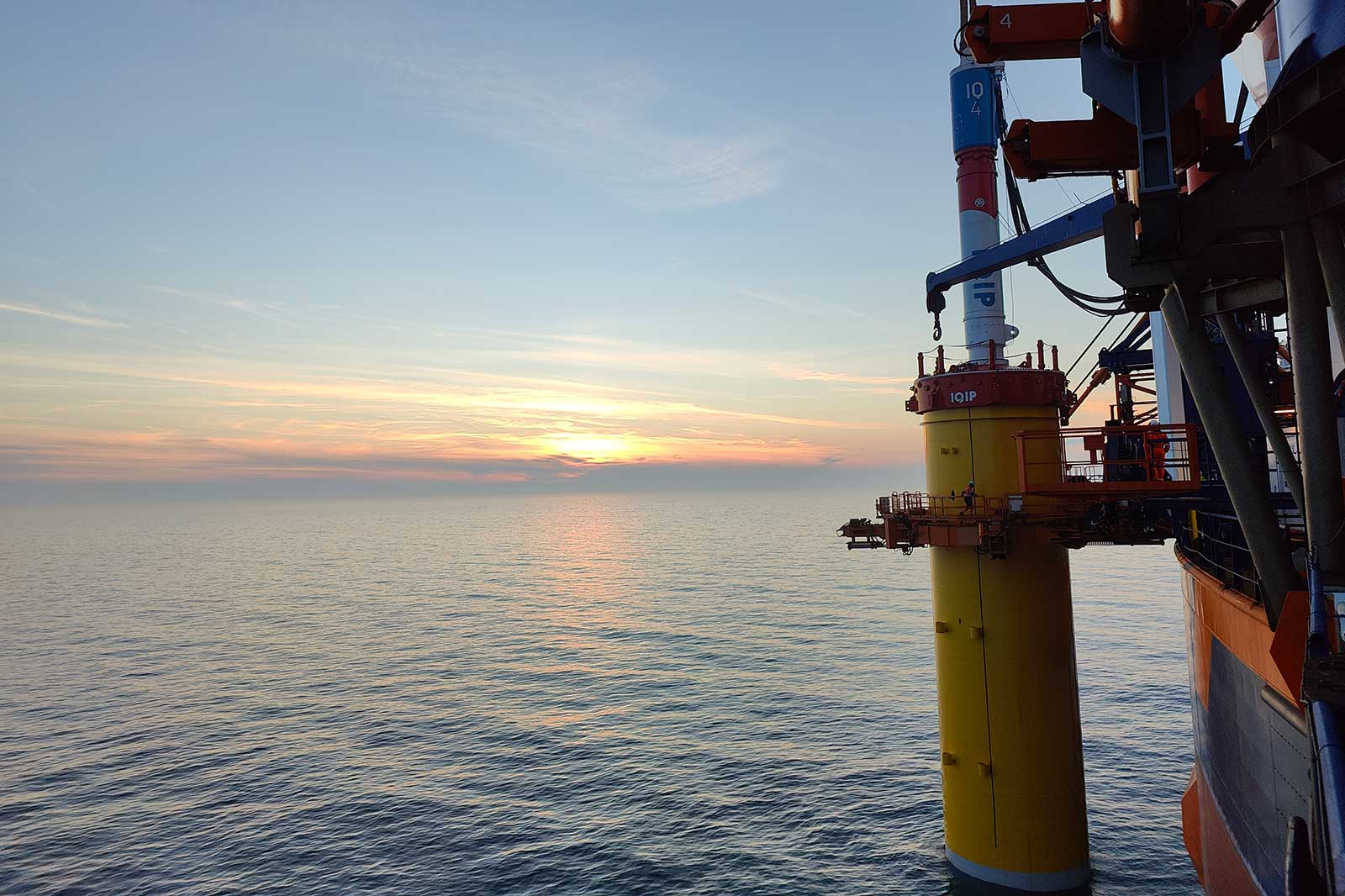 A vibrant sunset over calm sea waters with an offshore platform in the foreground.