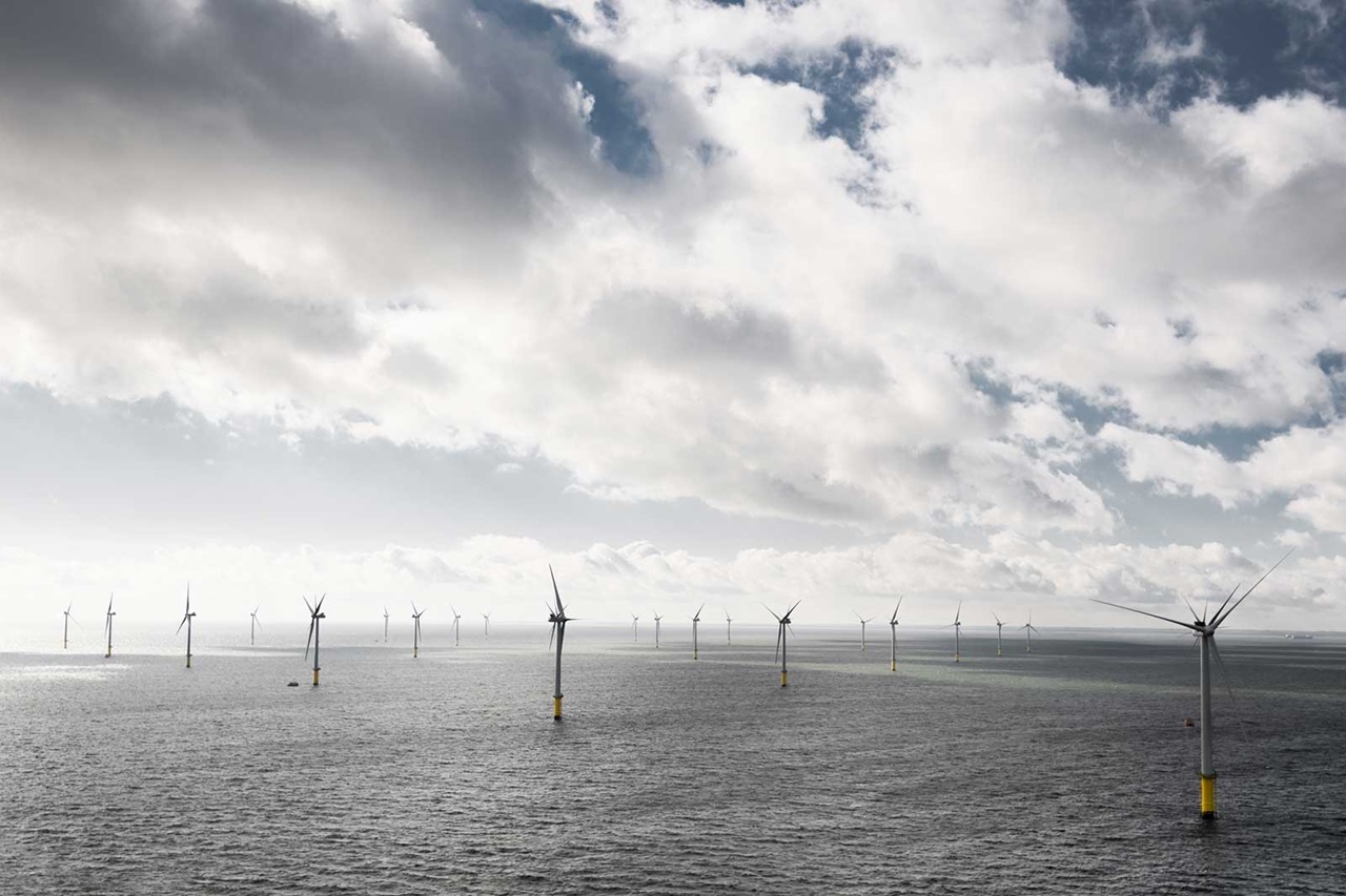 A row of wind turbines in the sea under a cloudy sky.