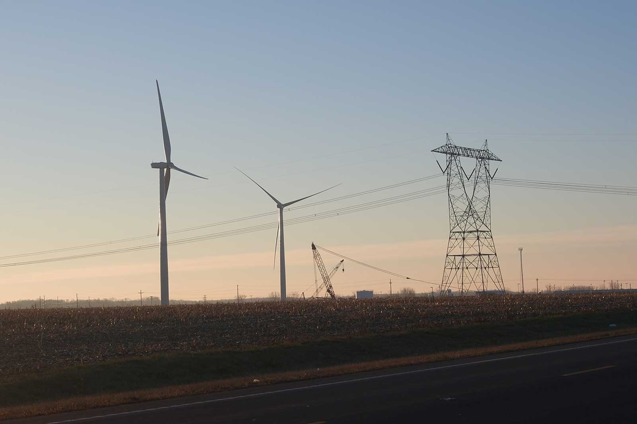 Wind turbines and power pylons in a rural setting at dawn, with a view of the road in the foreground.