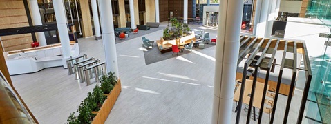 A modern lobby area featuring seating, plants, and a reception desk. Large windows provide natural light.