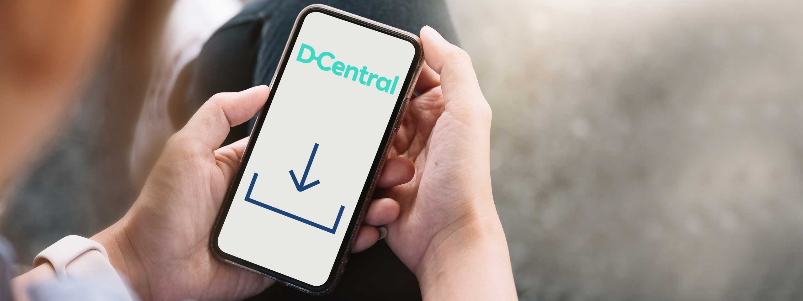 Eine Person hält ein Smartphone mit dem D-Central Logo und einem Download-Symbol auf dem Bildschirm.