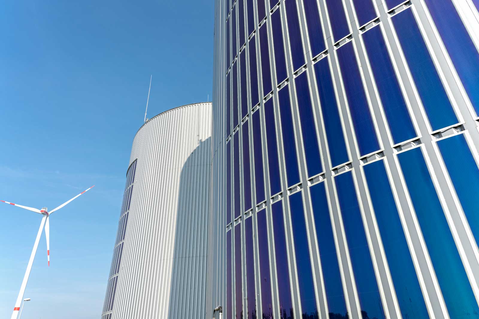 A modern building with reflective glass surfaces and a wind turbine in the background, set against a clear blue sky.