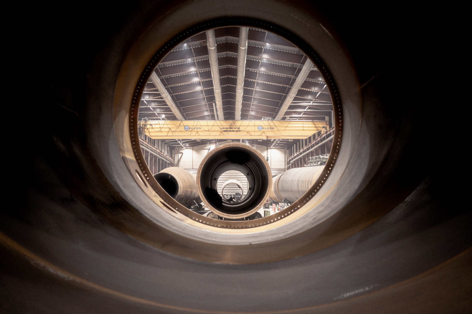 View through large pipes in an industrial hall, featuring a crane in the background and additional pipes in the space.