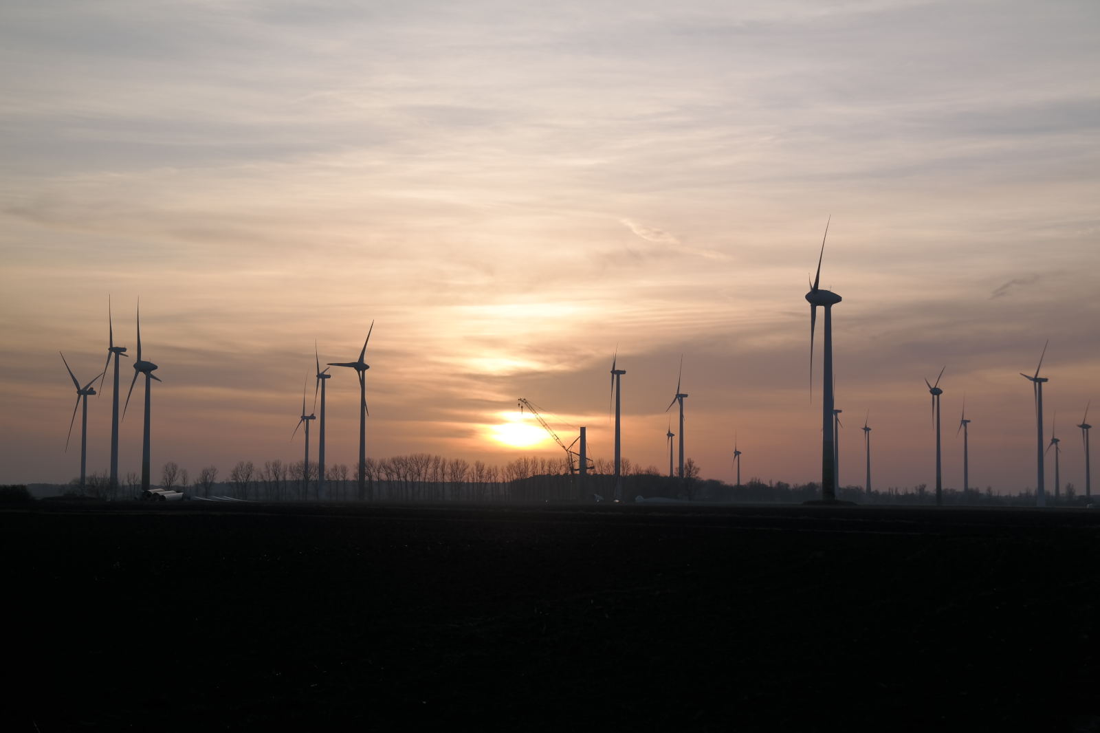 Eine ruhige Sonnenuntergangsansicht über einen Windpark mit mehreren Windkraftanlagen, die sich vor einem bewölkten Himmel abheben.