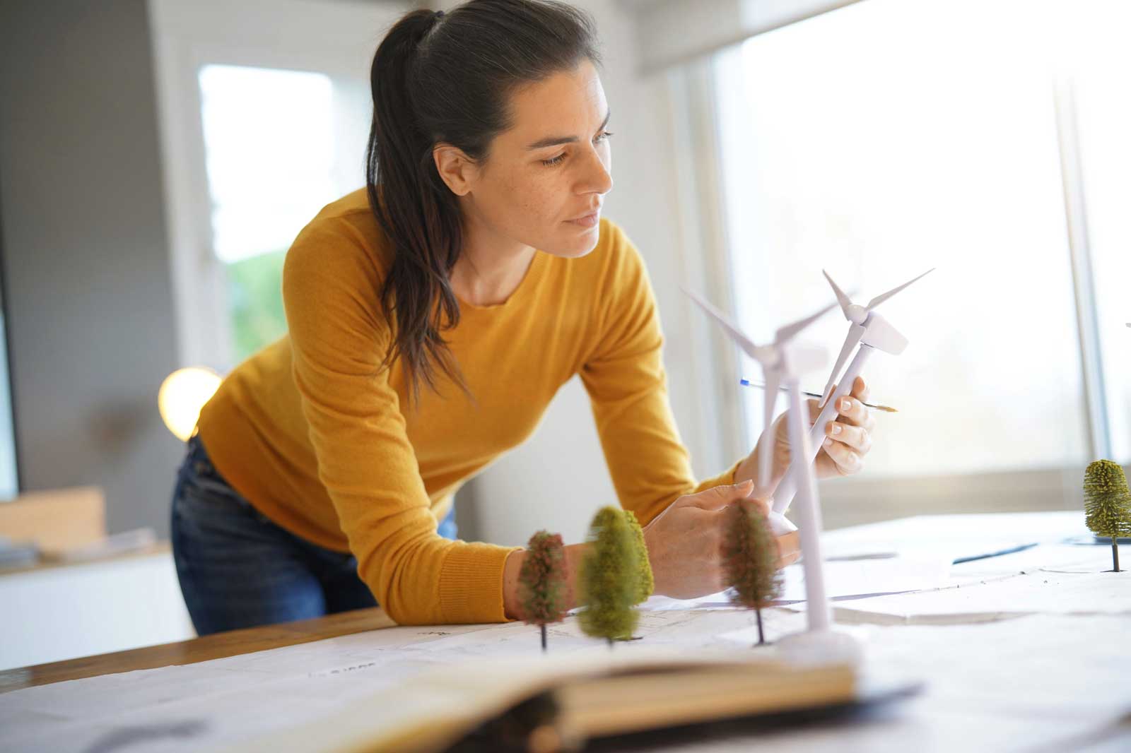 Eine Person in einem orangefarbenen Pullover betrachtet Windkraftanlagenmodelle auf einem Tisch.