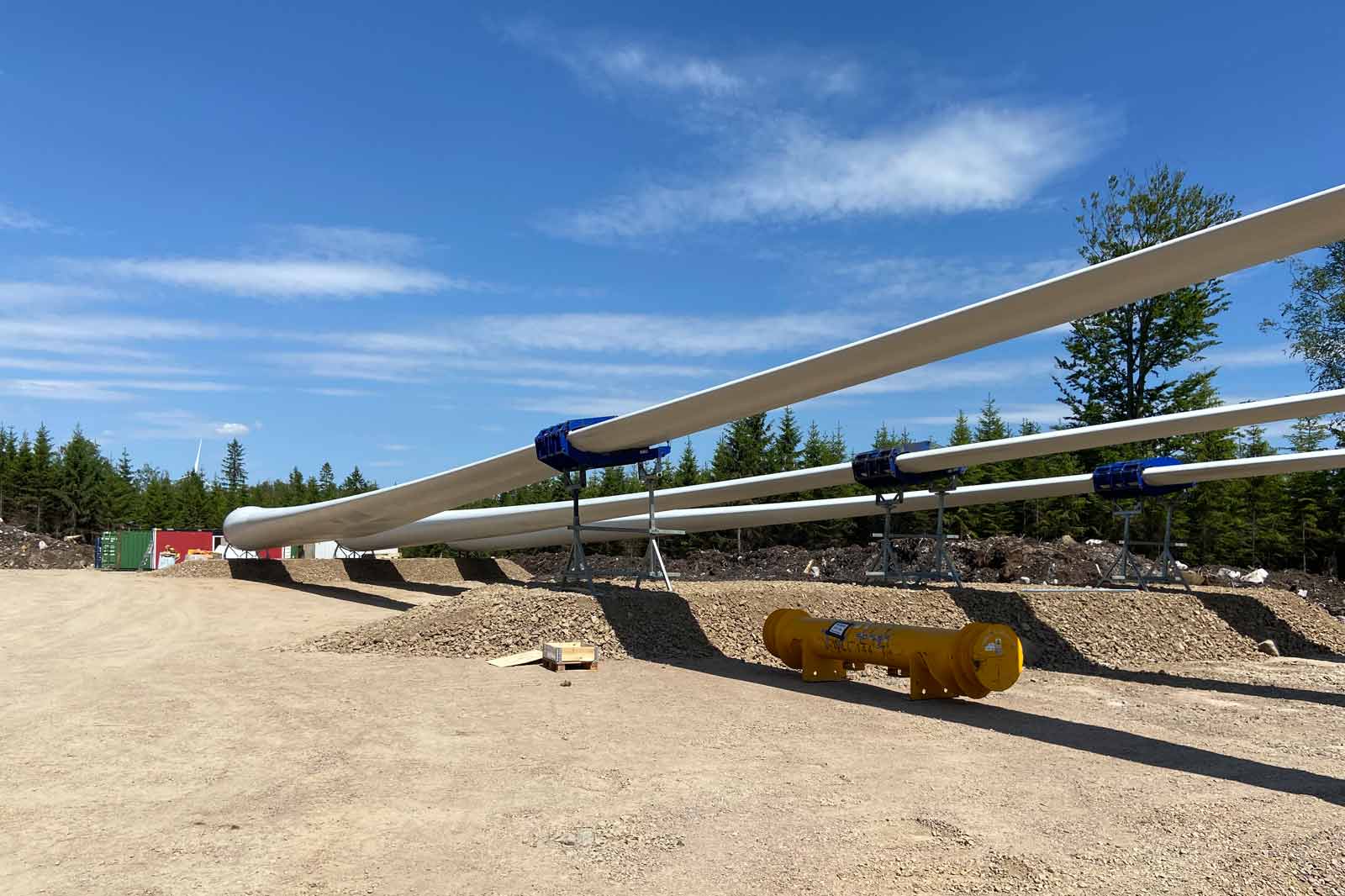 Auf dem Bild sind lange, weiße Rohre auf Holzständern in einem Kiesfeld zu sehen, mit einem blauen Himmel im Hintergrund.