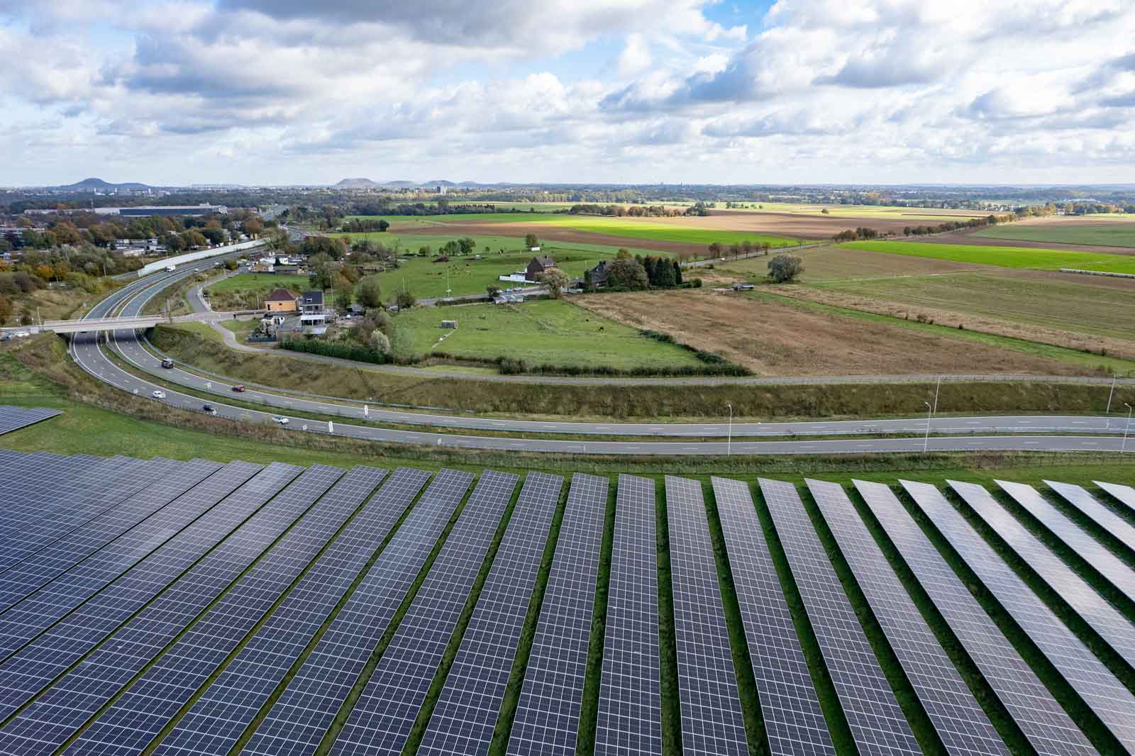 Eine große Solarfarm mit Solarpanelen im Vordergrund, umgeben von Feldern und einer Straße im Hintergrund.